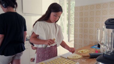 Genç kız ve oğlan mutfakta yemek pişirirken, kız da erkek izlerken hamur parçaları düzenlemeye odaklanmış. Bir öğrenme ve yaratıcılık anı.