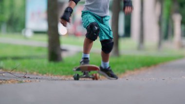 Kaykay yapan genç bir çocuğun yakın çekimi. Ayakları yerden havalanırken hareket ediyor. Dizlik ve bileklik takmak, asfalt yolda aktif bir açık hava macerası.