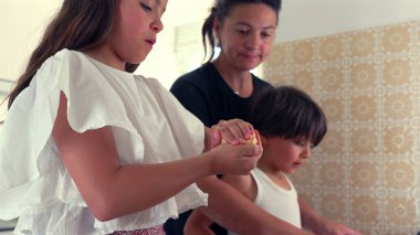 Anne ve oğlan arka planda izlerken, genç kız elleriyle hamuru şekillendiriyor. Bir dakikalık aile birlikteliği ve mutfakta öğrenme.