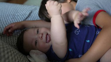 Ağabeyi bir kanepede bebek kardeşinin yanında yatarken sevgi dolu bir bağ ve şefkat anı yaşıyor. Her iki çocuk da sıcak bir ev ortamında sakin ve samimi bir zaman geçiriyor.