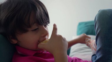 Kanepede uzanmış elma yiyen genç bir çocuğun rahat ve sakin bir yemek yeme ve tefekkür anındaki görüntüsü.
