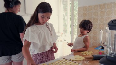 Genç kız ve oğlan mutfakta yemek pişirirken, kız da erkek izlerken hamur parçaları düzenlemeye odaklanmış. Bir öğrenme ve yaratıcılık anı.