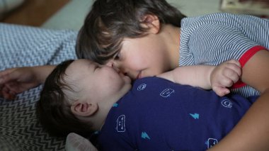 Ağabeyi bir kanepede bebek kardeşinin yanında yatarken sevgi dolu bir bağ ve şefkat anı yaşıyor. Her iki çocuk da sıcak bir ev ortamında sakin ve samimi bir zaman geçiriyor.
