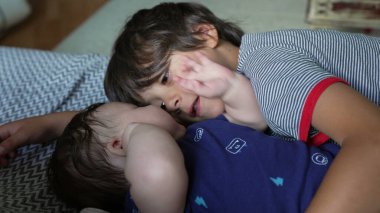 Ağabeyi bir kanepede bebek kardeşinin yanında yatarken sevgi dolu bir bağ ve şefkat anı yaşıyor. Her iki çocuk da sıcak bir ev ortamında sakin ve samimi bir zaman geçiriyor.