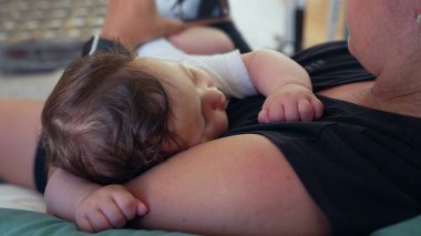 Bebek annesinin göğsünde dinleniyor, başı yana dönmüş, elleri hafifçe kıvrılmış, yakınlık ve konfor anı besleyici bir çevrede