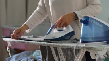 Gri kumaşı güvertede dikkatlice ütüleyen, günlük ev işlerini yapan, materyal, odaklanmış, metodik hareketin üzerinde düzgün bir şekilde süzülen demirin yakın plan görüntüsü