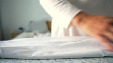 Beyaz kumaşı nazikçe katlayan eller, düzenli ve kesin hareketler, bir iç rutinin parçası, pürüzsüzlüğü ve organizasyonu sürdüren, odaklanmış ve sistemli görev