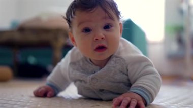 Bebek başını kaldırıyor ve ileriye bakıyor, odaklanmış ifade, elleri destekleyen vücut, erken emekleme aşaması, güç gelişimi, dikkatli bebek içeride, ev ortamında