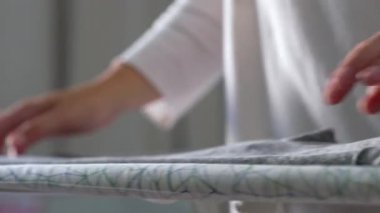 Yumuşak gri kumaşı ütü masasının üzerine katlayan ellerin yakın çekimi, metodik ve hassas hareketler, dikkatli katlama, tekstil organizasyonu, temiz ve düzenli hazırlık