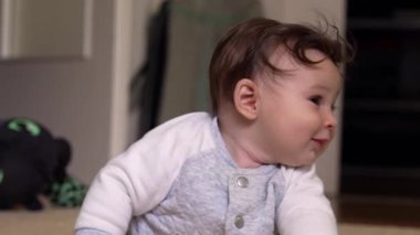 Bebek kollarını kavuşturup yerde uzanıyor. Ev ortamında huzur içinde dinleniyor.