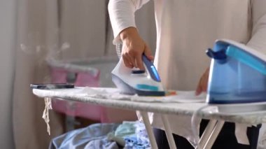 Ütü masasında el ele tutuşan demir, buharı tüten giysi, yumuşak baskı hareketi, bakım ve hassasiyete odaklanma, iç giysi bakımının rutini, temizliği ve pürüzsüzlüğü koruma