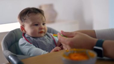 Bebeğin ilk kez katı yiyecekler denediği yakın plan, hafif isteksiz yüz ifadesi, ağız yakınında kaşık, ev dekorasyonu, yeni tatlara nazikçe giriş, bakım.