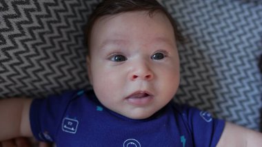 Bebeğin yakın plan bir kanepeye uzanmış, gözleri sonuna kadar açık, merak ve sakinliği ifade eden, rahat bir ev ortamında sessiz ve huzurlu bir anın tadını çıkaran