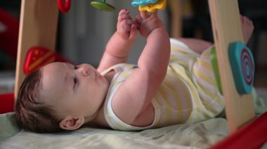 Bebek renkli oyuncakların altında yatar, asılı nesnelere bakar, duyusal keşiflere ve oyuncu keşiflere girişir, evde büyüyen bir ortama odaklanır.
