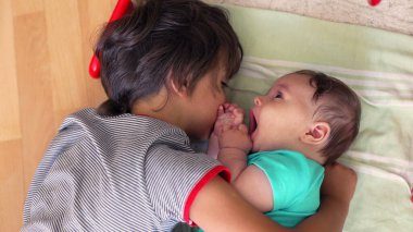 Küçük çocuk, bebek kardeşinin yanında yatıyordu, ikisi de sakin bir bağ anında yerde yatıyordu, bebek çocuğa bakıyordu, huzurlu bir ev ortamında sevgi ve bağlantı gösteriyordu.