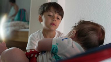 Küçük bir çocuk, bir fedainin içinde kardeşiyle konuşuyor, sıcak bir etkileşim ve bağlantı anına bağlanıyor, aile ortamında kardeş bağını teşvik ediyor.