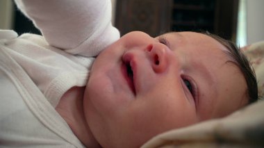 Sakin bir ifadeyle bebek bakışı, sıkıca kavrayan parmaklar, bebek hoşnut ve meraklı görünüyor, yumuşak ten ve odakta narin özellikler