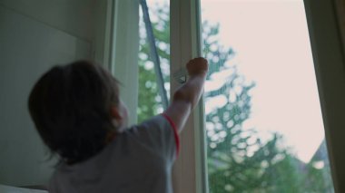 Genç çocuk başarılı bir şekilde bir pencere açıyor, başarı ve merak anı, açık hava manzaralı kapalı bir sahne, çocuk çevreyi keşfediyor ve onunla etkileşime geçiyor.