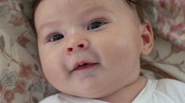 Yumuşak gülüşlü, çiçekli battaniyeye uzanmış bebek, rahat ve hoşnut görünüyor, bebek merakla bakıyor, huzurlu ve neşeli bebek huzur içinde dinleniyor.