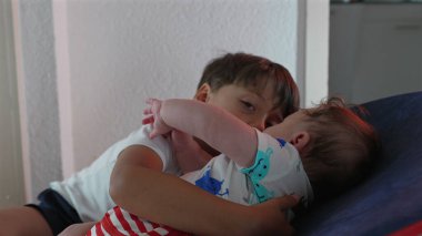 Küçük bir çocuk, bir fedainin içinde birlikte otururken kardeşine sarılıyor. Evde şefkatli bir kardeş gibi sevgi ve özen gösteriyor.