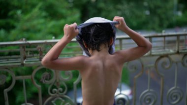 Genç bir çocuk balkonda dikilirken tişört giyer, dünyaya bakar, düşüncelere dalıp hazırlanır, yerleşim alanındaki huzurlu bir açık hava sahnesine çıkar.