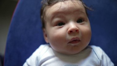 Bebeğin kameraya doğrudan meraklı gözlerle bakması, çevreyi gözlemlemesi, sakin ve meraklı ifade, erken gelişimi yakalamak ve bebeğin dikkatini çekmek.