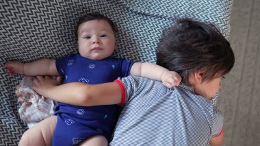 Bebek, ağabeyinin yanında kanepede yatar, bebek, kardeşinin kollarında dinlenir, sıcak bir yuvada sevgi ve yakınlık anlarını gösterir.