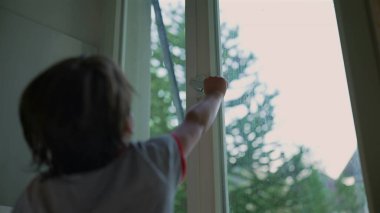 Genç çocuk başarılı bir şekilde bir pencere açıyor, başarı ve merak anı, açık hava manzaralı kapalı bir sahne, çocuk çevreyi keşfediyor ve onunla etkileşime geçiyor.