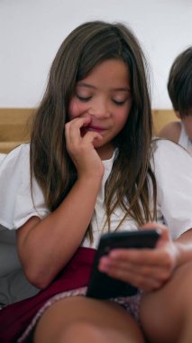 Akıllı telefon ekranına bakarken tırnağını yiyen genç bir kız odaklanmış konsantrasyonunu ve elinde cihazla dijital bir göreve girişini gösteriyor.