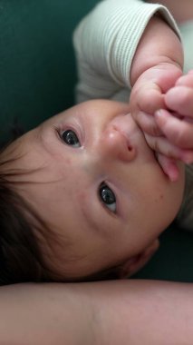 Kanepeye uzanmış, elleri ağıza yakın bir şekilde yukarıya bakıyor. Huzurlu ve sakin bir bebek gibi, besleyici bir ortamda.