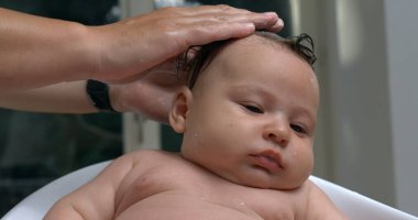 Hand gently washing baby head with water during bath, baby calm and relaxed, water droplets visible on head, intimate bath care moment, soothing gesture. 800 fps slow-motion clipart