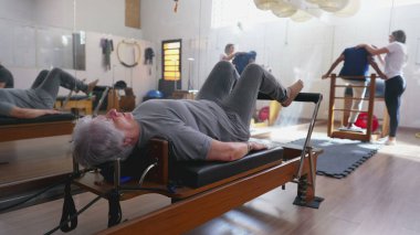 Pilates Stüdyo Makinesi 'nde beden egzersizi yapan yaşlı bir kadın. Kafkasyalı yaşlı bir kadın omurga sağlığıyla ilgileniyor..