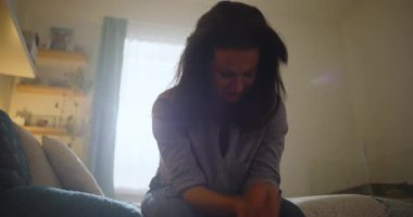 Elleri havada bir kadın, duygusal çöküntü içinde yatakta oturuyor, özel ve düşünceli bir an, üzüntü ve stresle mücadele ediyor, iç mekan ışığını bastırıyor.