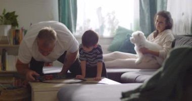 Aile, sıcak oturma odasında birlikte vakit geçirir. Büyükbaba, küçük çocukla oynar. Anne, evcil köpekle kanepede gülümser.