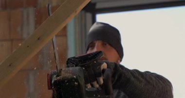 Elektrikli testereyle odun kesen işçiler, 800 fps hızla uçan odun kıymıkları, odaklanmış ifade ve sağlam eller, kapalı alanda ahşap kesme hassasiyeti.