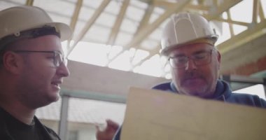 İnşaat halindeki bir binanın içindeki mimari planlara odaklanan üç inşaat işçisinin yakın çekimi, ekip çalışması ve proje ayrıntılarına dikkat edilmesi