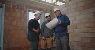 İnşaat ekibi, bitmemiş bir binanın içindeki planları gözden geçirir, inşaat projesinin tasarımını koordine eder ve mimari ayrıntıları tartışır.