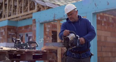 İnşaat alanında elektrikli testere kullanan işçiler havada uçuşan ahşap talaşları, hassas kesimler, açık hava inşaat işleri.