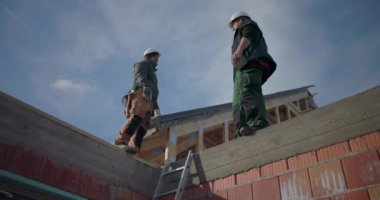 Çatıda projeyi tartışan iki inşaat işçisi, kask takıyorlar, konut inşaatı projesinde takım çalışması yapıyorlar, iletişim ve işbirliğine odaklanıyorlar.