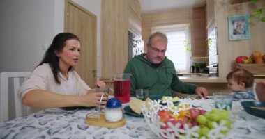 Aile yemek masasında birlikte kahvaltı yapıyor, anne bir bardak meyve suyu tutuyor, baba çocuklara yardım ediyor, sevgi ve sevgi besliyor.