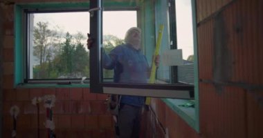 Elle çalışan kişi, konut inşaatı alanındaki pencere montajını, çerçeve hizalamasını ve güvenli kurulum için kalite standartlarını denetliyor