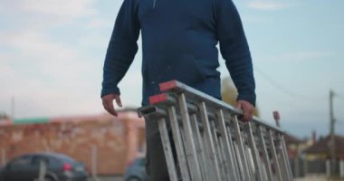 İnşaat alanında alüminyum merdiven taşıyan işçiler, açık hava görevine hazırlanıyor, yenileme ve inşaat işleri için araç ve ekipmanın vurgulanması