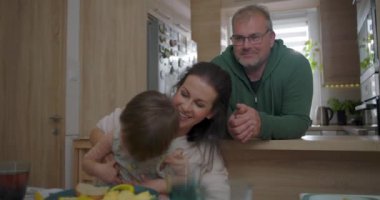 Anne büyük çocukla yemek masasında gülerken, baba izliyor, neşeli aile anı sıcak yuva ortamında bağ ve mutluluk yaratıyor.