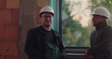 Sert şapkalı inşaat işçileri geniş bir pencerenin, rahat atmosferin, kapalı inşaat alanının, takım çalışmasının ve günlük etkileşimin yanında hafif bir sohbet paylaşıyorlar.