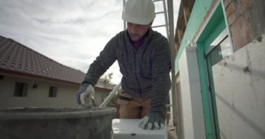 Kovadan havan topu çıkarmak, dış duvardaki yalıtım işleri için güvenlik donanımlı inşaat işçisi, arka planda kask, eldiven ve merdiven ile yakın plan.