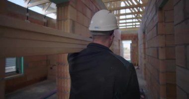 İnşaat işçisi, tamamlanmamış binanın dar koridorunda omuzlarında uzun tahta kiriş taşıyor. İnşaat alanında işçilik ve takım çalışması sergiliyor.