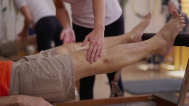Pilates koçu hastaya rehberlik ediyor. Makineyle bacaklarını güçlendiriyor. Mutlu fizyoterapist iş hizmeti kişinin daha iyi fiziksel sağlığına kavuşmasına yardımcı oluyor..