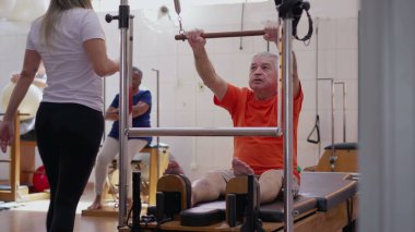 Pilates eğitmeni yaşlı bir adamın makine, egzersiz, sağlık ve sağlık yaşam tarzını kullanmasına yardım ediyor..