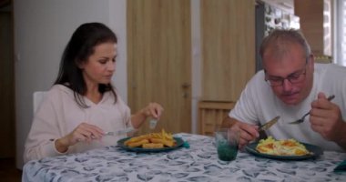 Ebeveynler ve çocuklar masada yemeklerini yiyorlar, aile bağlarını ve sıcak ve davetkar bir mutfak ortamında rutinlerini paylaşıyorlar.
