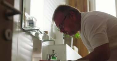 Banyodaki lavabodan gelen suyla ağzını çalkalayan adam, parlak ve temiz minimalist ortamda ağız hijyenine ve özgüvenine odaklanıyor.